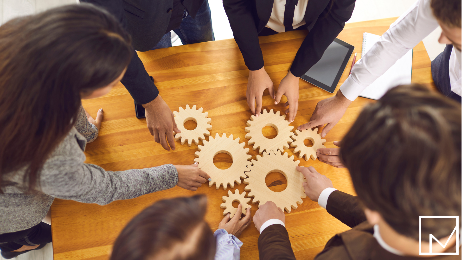 Business professionals holding interlocking wooden gears over a table, symbolizing teamwork and collaboration.