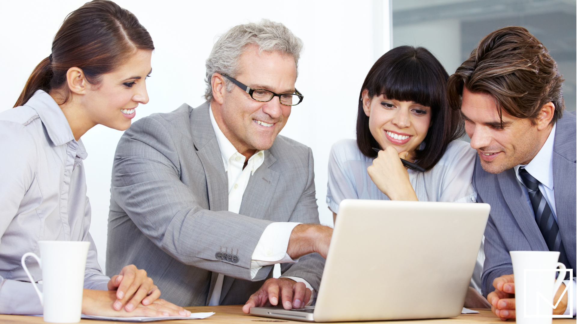 Businessman pointing at laptop screen in a boardroom meeting with three colleagues attentively looking on.