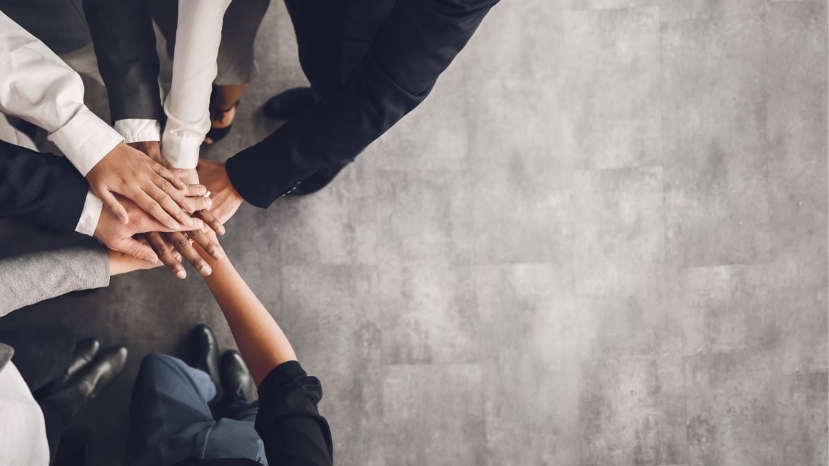Team stacking hands together in office, representing internal investment and collaboration to scale a staffing business.