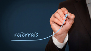 Man’s hand drawing the word 'referrals' inside an upward-pointing arrow on a whiteboard.