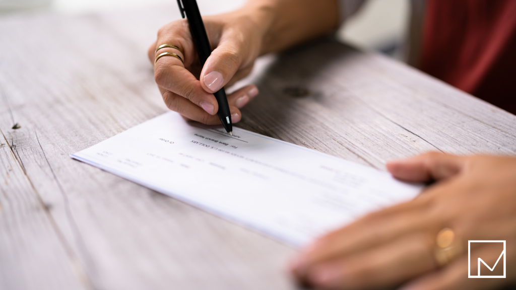 A person writing a check with a pen, symbolizing obtaining a loan, representing the concept of payroll funding versus bank loans.
