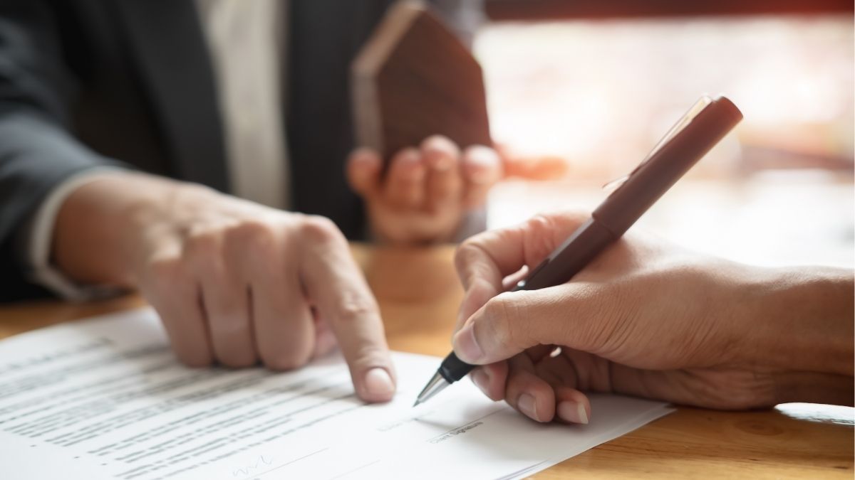 Person signing a financial agreement while another points to the document, representing the decision between payroll funding and bank loans for staffing agencies.