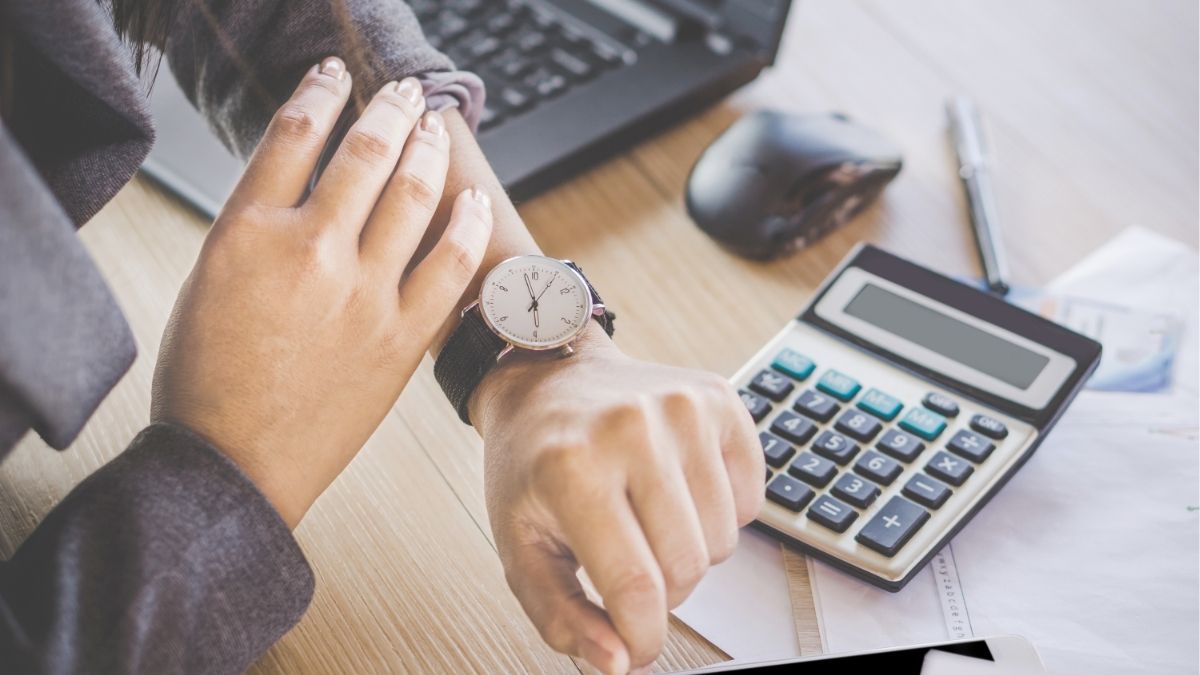 Professional checking watch beside calculator and laptop, representing time management and financial planning for staffing agency operations.
