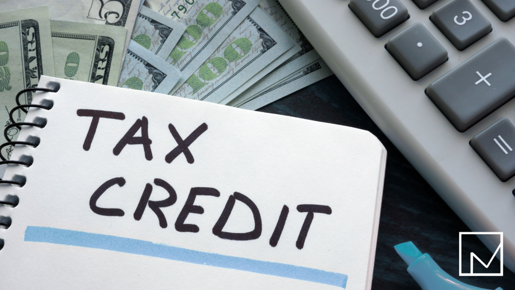 Visualizing tax credit benefits: A sticky note labeled 'Tax Credits', a calculator, and dollar bills highlight financial advantages like the EITC.