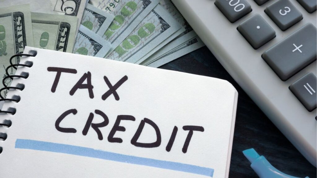 Notebook labeled “Tax Credit” next to cash and calculator, representing the Earned Income Tax Credit and its financial benefits for staffing firms and employees.