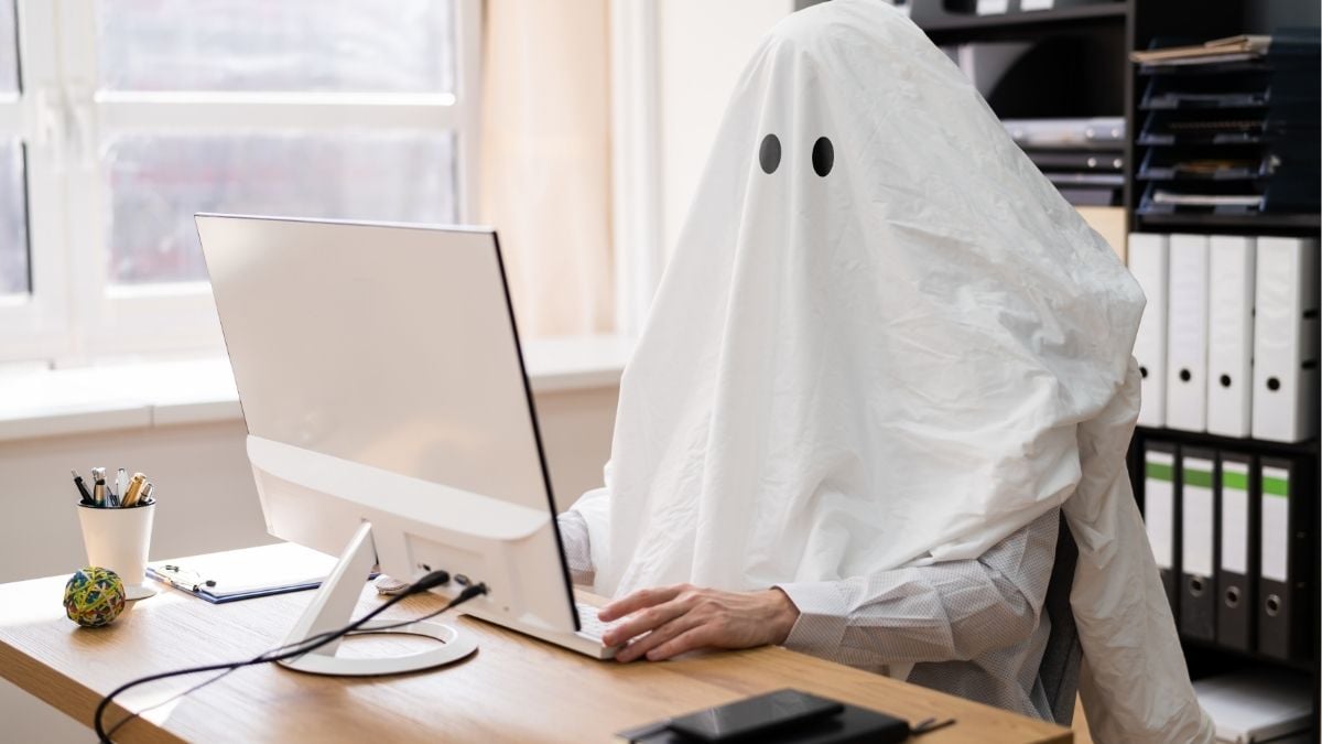 Person dressed as ghost working at computer representing candidate ghosting in the job market.