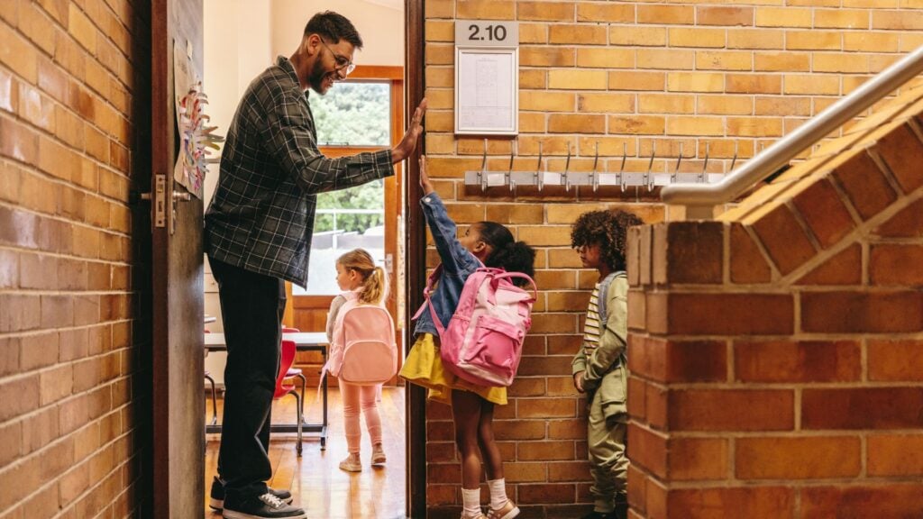Teacher welcoming students into a classroom, representing education staffing support and school-based placements.