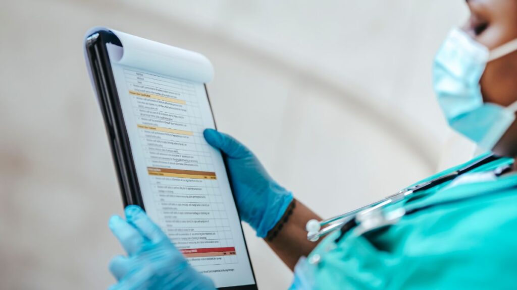 Nurse wearing a face mask reviewing a clipboard in a hospital setting, representing healthcare staffing cash flow challenges and workforce management.