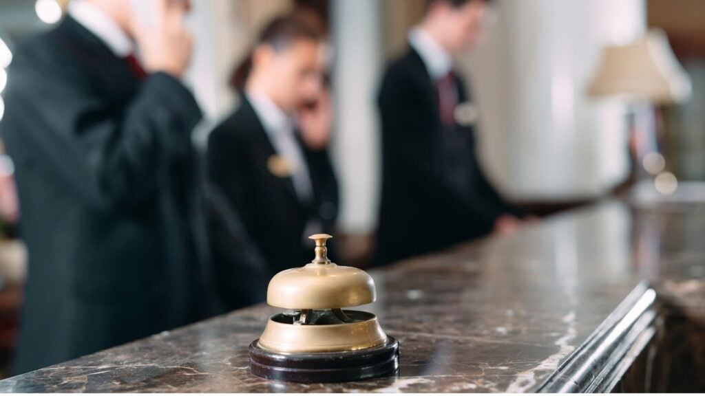 Hotel front desk bell with hospitality staff in background, representing hotel staffing operations and workforce management.