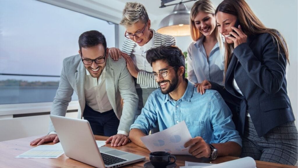 Team collaborating around laptop reviewing data, representing integrated staffing solutions including payroll funding, back office support, and reporting working together to drive growth.