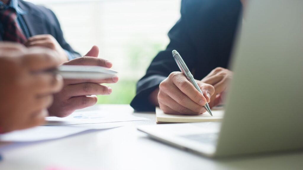 Professionals reviewing documents and taking notes in a meeting, representing strategic consulting and advisory for office and clerical staffing firms.
