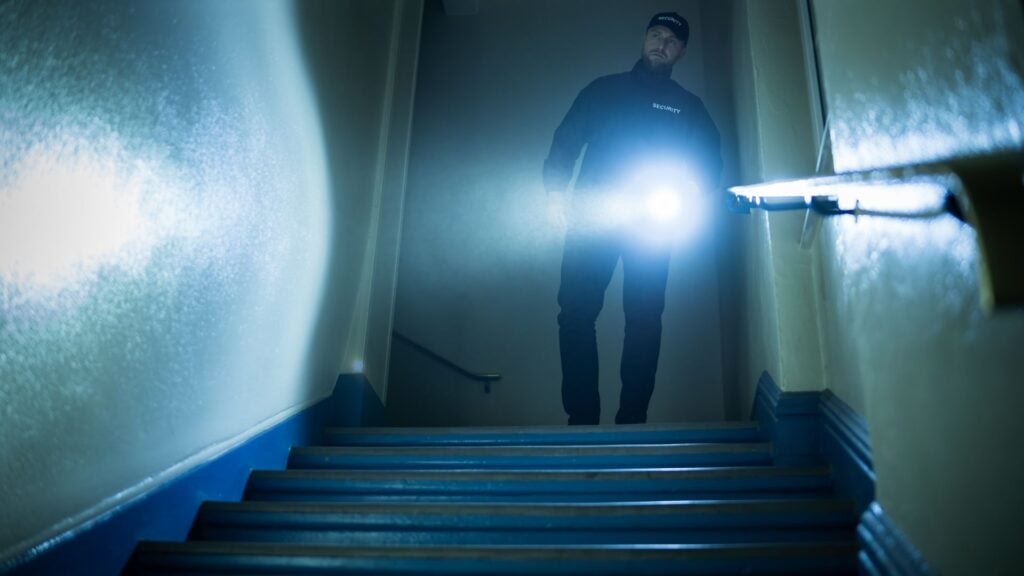 Security guard performing a night patrol with flashlight, representing 24/7 security staffing and on-site protection services.