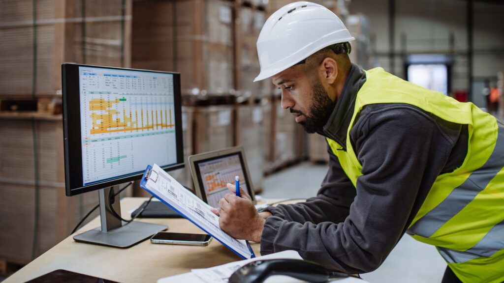 Warehouse employee reviewing staffing and payroll data in a distribution center representing payroll funding for light industrial staffing firms.