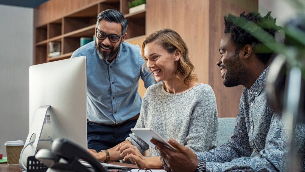 Staffing professionals collaborating around a computer representing software solutions, operational support, and scalable growth for staffing firms.