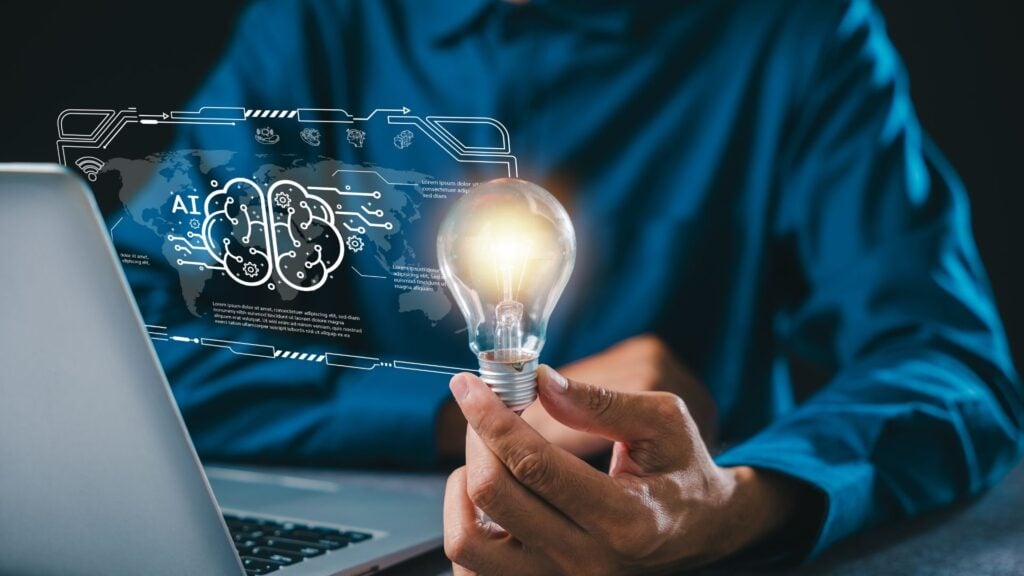 Person holding a glowing light bulb in front of a laptop with a digital AI brain interface, representing AI adoption in staffing, innovation, technology implementation, and building trust in artificial intelligence solutions.