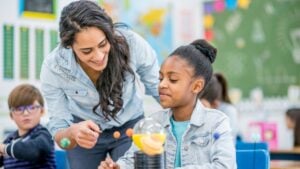 Teacher helping an elementary student with a solar system model in a classroom.